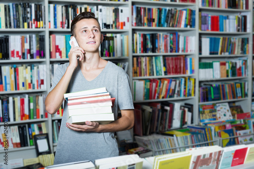 Boy holding books and talking on mobile phone in shop © JackF