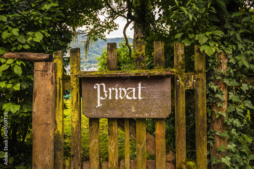 Vintage private sign in german language on an old wooden gate grown with moss and ivy and surrounded by trees.