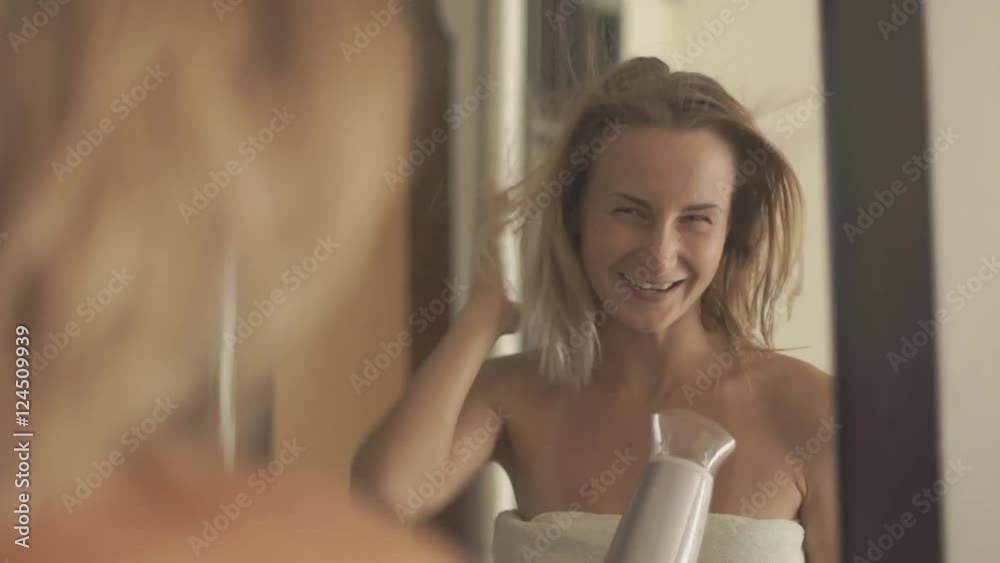 Woman drying her hair in bathroom in front of a mirror.