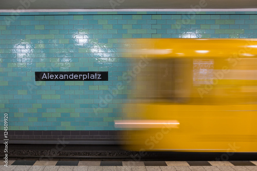 Yellow subway train in Motion. Berlin Alexanderplatz sign visible on the wall of underground station.