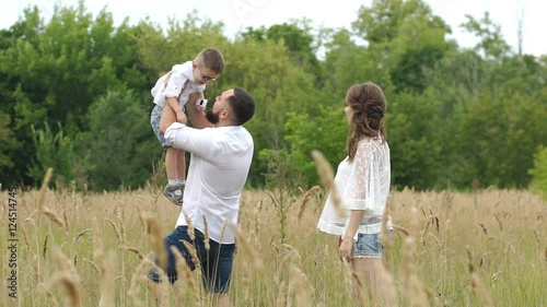 Happy family walking outdoor. Parents hold child on hands and rejoice photo