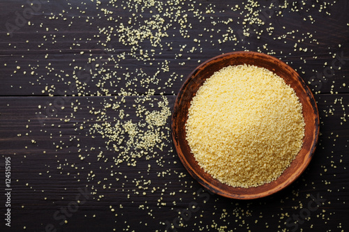 Raw couscous in bowl on dark wooden background from above photo