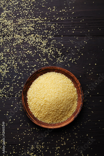 Raw couscous in bowl on dark rustic background from top view