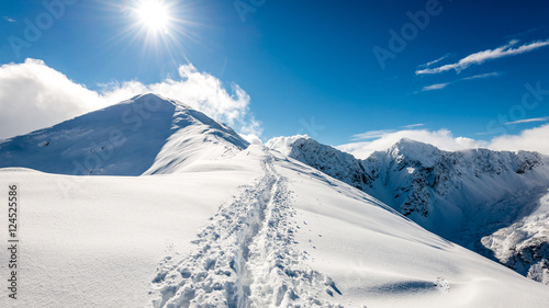 mountain tops in winter covered in snow with bright sun and blue © Martins Vanags