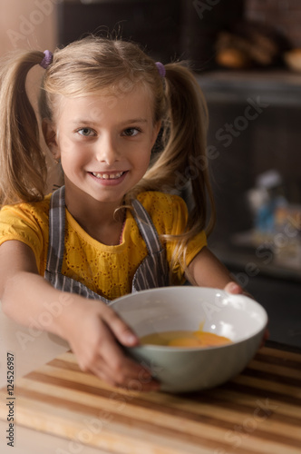 Smiling little girl holding the bowl with broken eggs