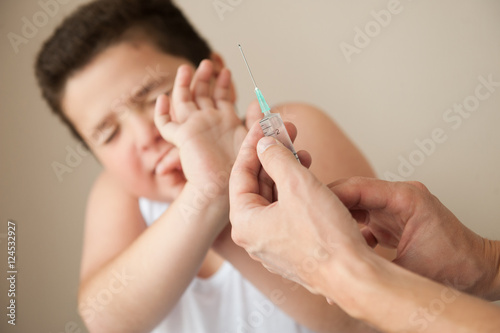 fat little boy covered his face from hands with syringe