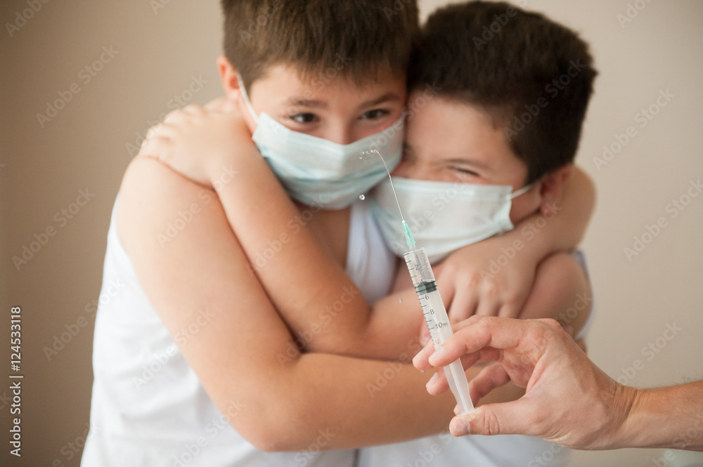 two scared boys in medical mask looking at hand with syringe