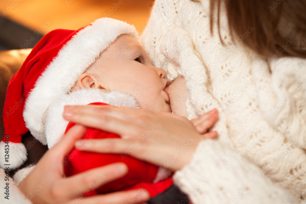Newborn baby wearing as Santa Claus breast feeding. Selective focus on the kid s face. Homemade Christmas Newborn baby wearing as Santa Claus breast feeding. Selective focus on the kid s face. Homemade Christmas
