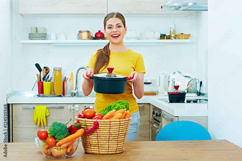 Smiling woman in kitchen holding pan.