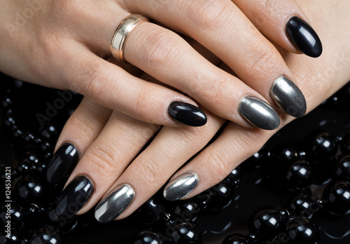 Beautiful female hands with nail polish black and silver color with black and silver beads on a black background