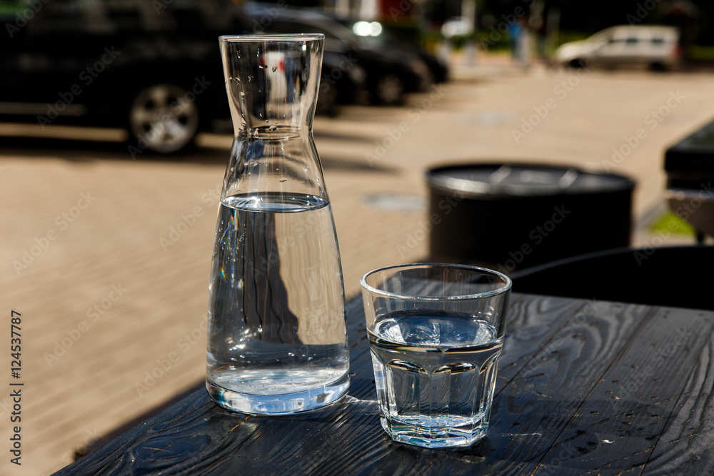 A glass of water and a water-bottle on a black wooden table of a city cafe terrace