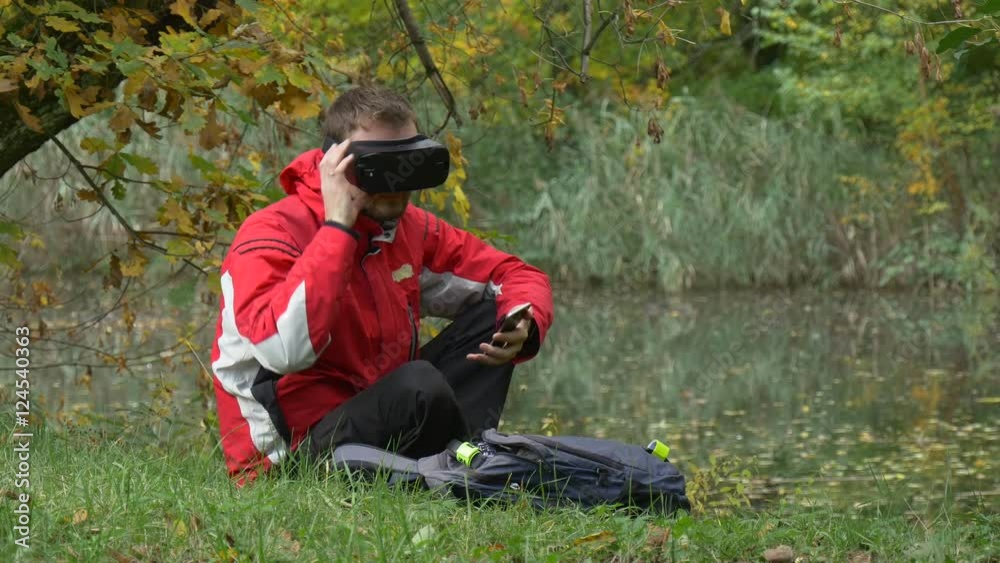 Man Watching Video 360 Degrees in vr Glasses Using Smartphone Clicks the Device Removes the Headset Put it on Again Playing Virtual Games in Park by Water Man Watching Video 360 Degrees in vr Glasses Using Smartphone Clicks the Device Removes the Headset Put it on Again Playing Virtual Games in Park by Water
