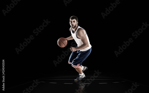 Professional basketball player holding ball on black background
