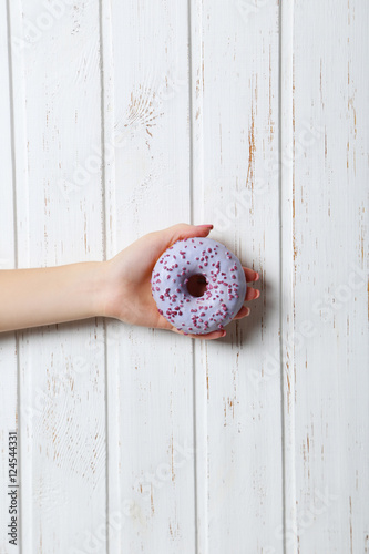 Female hand holding sweet donut on wall paneling background