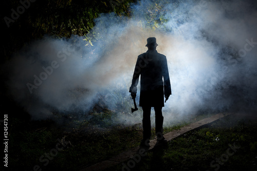 spooky man wih axe in the dark smoke filled forest photo