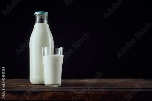 Full bottle of milk beside cup with copy space