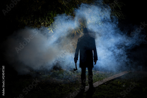 spooky man wih axe in the dark smoke filled forest photo