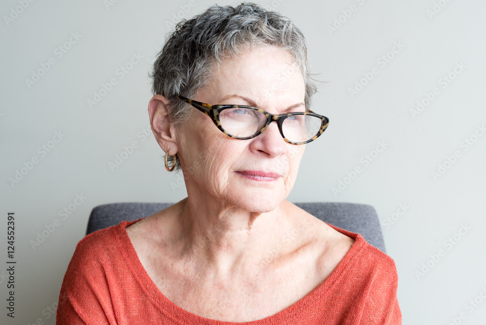 Older woman in orange top with glasses looking thoughtful against neutral background