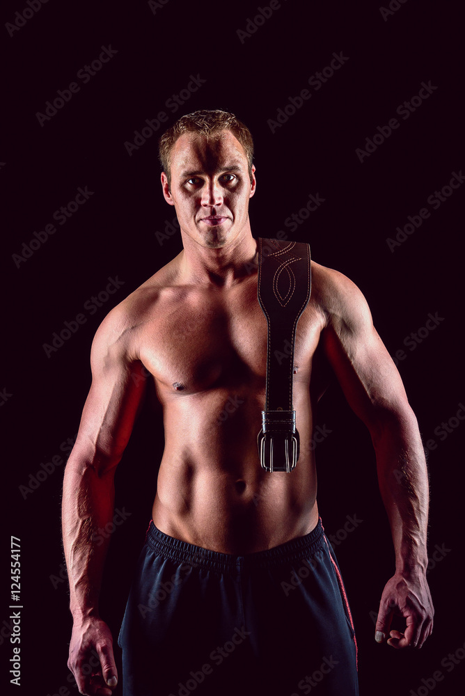 Muscular man in with lifting belt posing over dark background.