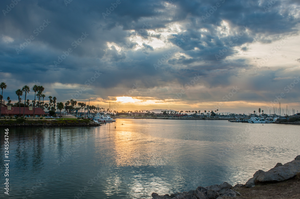 Stormy clouds over Ventura Harbor mouth lets spot of sun down on kayaker.