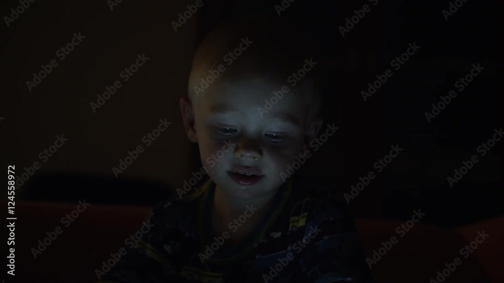 A young boy watches a tablet in the darkness. 4k. A young boy watches a tablet in the darkness. 4k.