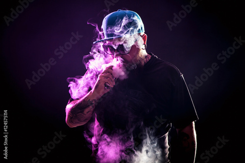 Men with beard  in sunglasses vaping and releases a cloud of vapor. photo