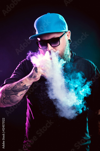 Men with beard in sunglasses vaping and releases a cloud of vapor.