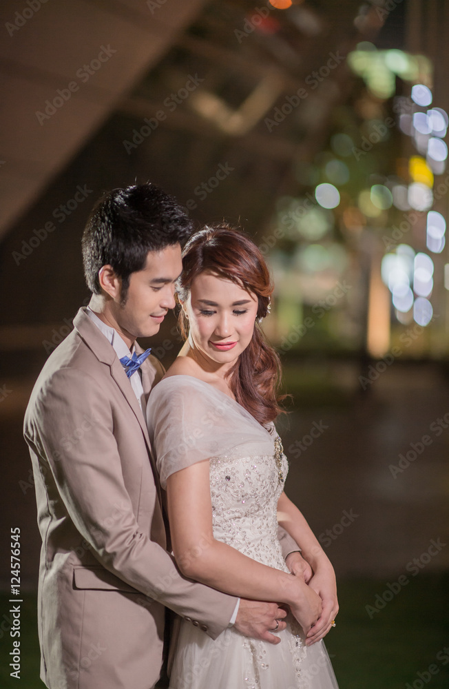 Happy newlywed groom hugging and kissing blonde beautiful bride at night in city Happy newlywed groom hugging and kissing blonde beautiful bride at night in city