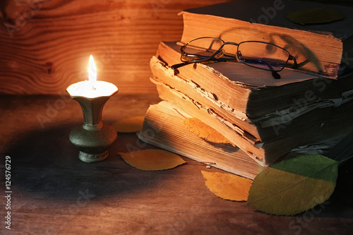 old tattered book on a wooden table lighted candle and glasses