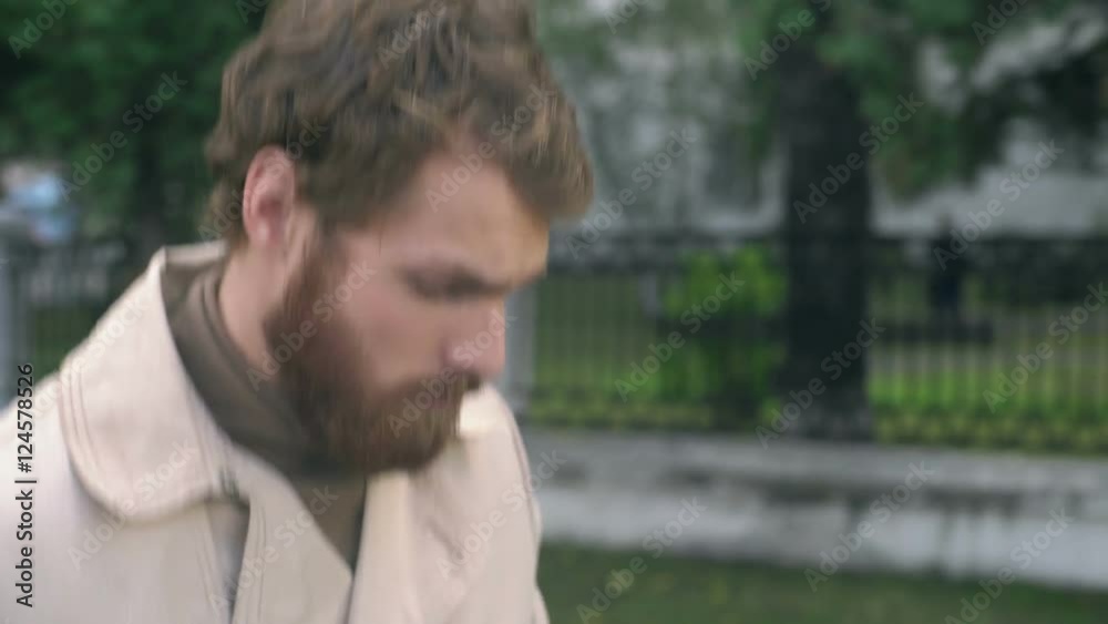 Tracking with tilt up of young man with beard walking along street and typing on phone, people with gadgets in background Tracking with tilt up of young man with beard walking along street and typing on phone, people with gadgets in background