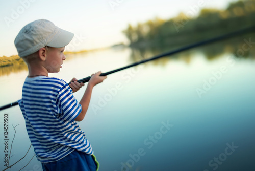 little boy in a cap fishes a fishing tackle in the river in summer