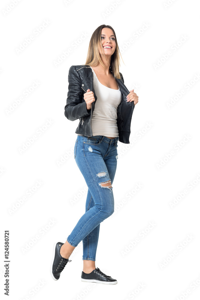 Gorgeous young beauty in ripped jeans and leather jacket looking up smiling. Full body length portrait isolated over studio white background. Gorgeous young beauty in ripped jeans and leather jacket looking up smiling. Full body length portrait isolated over studio white background.
