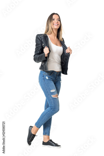 Gorgeous young beauty in ripped jeans and leather jacket looking up smiling. Full body length portrait isolated over studio white background.