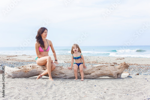 Fotografía Beautiful brown haired woman sitting on the beach with her blonde child