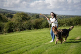 Teenage girl plays with her dog outside in a field. She is throwing the ball and playing fetch.