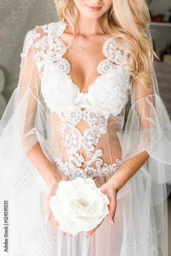 A portrait of a young bride in a lace underwear holding a huge white flower, blonde wavy hair on her shoulder
