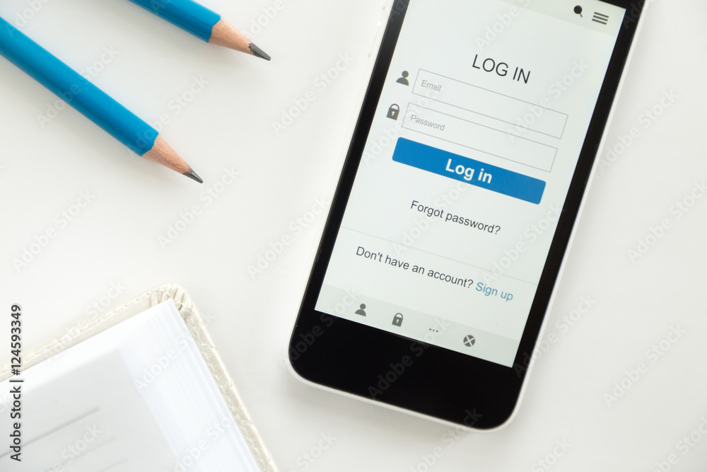 Top view of a mobile phone lying on a white office desk, log in on the screen, part of a notebook, sharp pencils, blue color. Business concept, lay flat