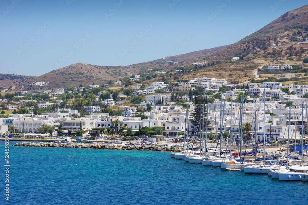 Sailing boats are docked on the coast of a small town of white houses, greek islands in the sunny day of summer