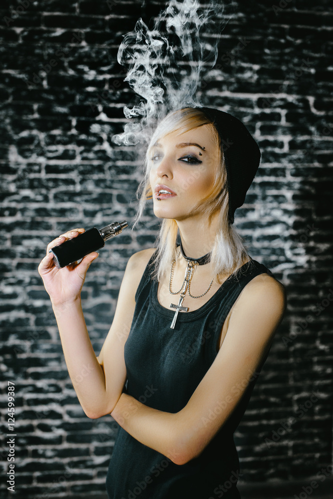 Sexy goth girl smokes electronic cigarette on dark background. The model  vaper vaping a vaporizer in the studio. foto de Stock | Adobe Stock