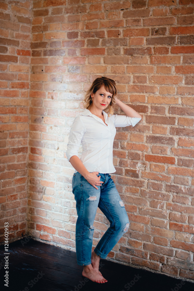 pretty girl in a white shirt and blue jeans against a brick wall 