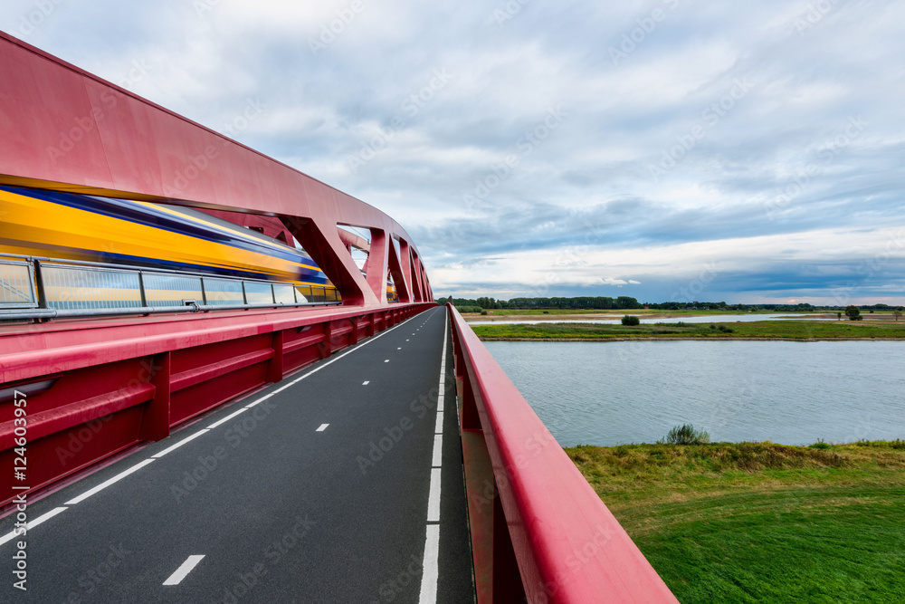 Naklejka premium Dutch Double Decker Train crossing the IJssel River going over contemporary Hanzeboog railway bridge.