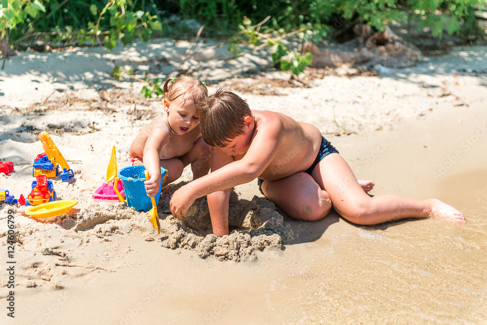 Children playing on the beach, build sand castles, sunbathing. Summer vacation. Parenting and child entertainment.