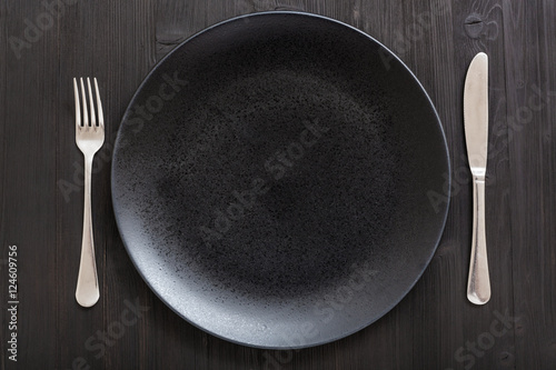 top view of black plate with knife, spoon on dark