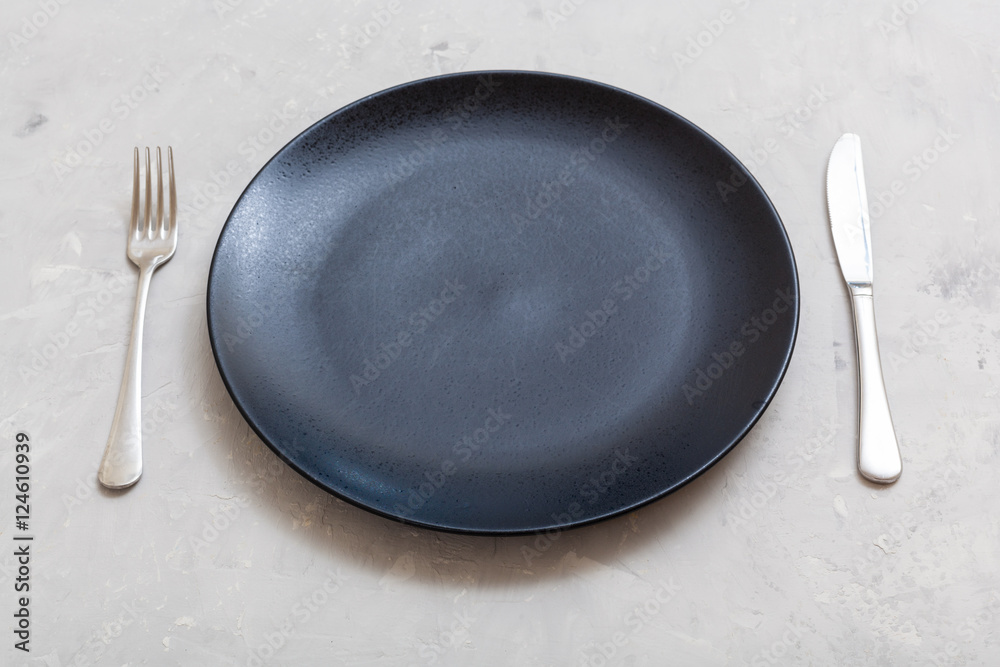 black plate with knife, spoon on gray concrete black plate with knife, spoon on gray concrete