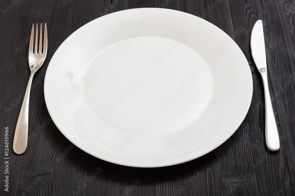 white plate with knife, spoon on dark brown table