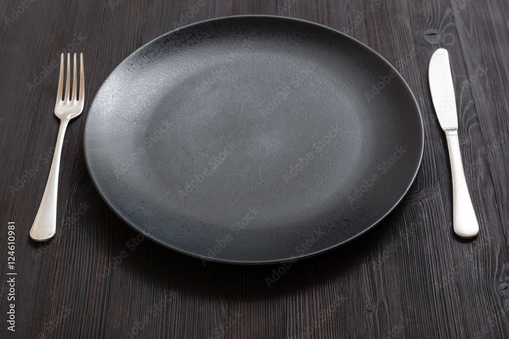 black plate with knife, spoon on dark brown table black plate with knife, spoon on dark brown table