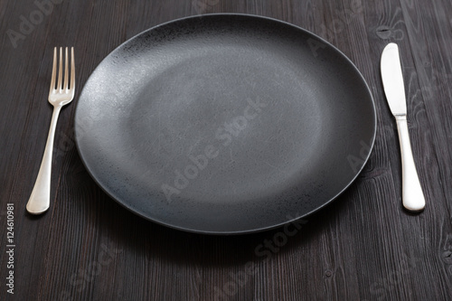 black plate with knife, spoon on dark brown table