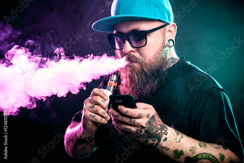 Men with beard  in sunglasses vaping and releases a cloud of vapor.