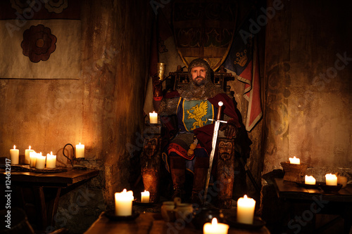 Medieval king on throne in ancient castle interior.