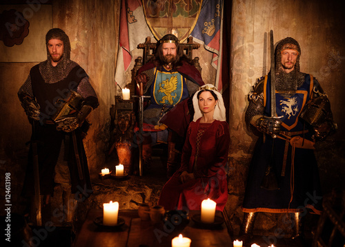 Medieval king with his queen and knights on guard in ancient castle interior